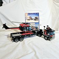 Full assembled LEGO set including truck, trailer, helicopter, with instruction manual visible in background.