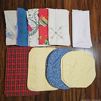 Display of various folded napkins and placemats including plain white, patterned, and embroidered items.