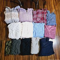 Photo of assorted tops and hoodies laid out on wooden floor showing a variety of colors and patterns including floral, plaid, and solid colors