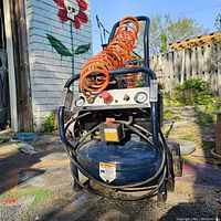 Front view of Mastercraft air compressor showing control panel with gauges, safety valve, and orange coiled air hose on top.