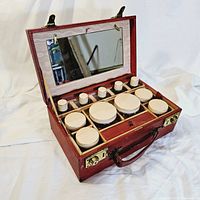Open ruby red leather vanity case with removable standing mirror and 11 glass containers with cream lids inside.