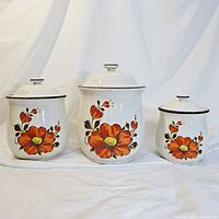 Photo showing full set of three vintage white ceramic canisters with orange poppy floral designs, lids on, varying sizes.