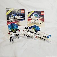 Both Lego sets with their original instruction booklets, showing the hovercraft and strategic pursuer models with minifigures in front of their manuals.
