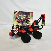 Side view of complete red and black Lego M-Tron Celestial Forager rover with mini figure and instruction manual behind