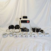 Full lot display showing MultiChef Espresso/Cappuccino Maker, various espresso mugs and matching saucers arranged in rows with brand logos visible.