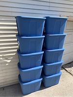 Stack of 10 blue storage tubs outdoors against a white house wall, showing size and quantity.