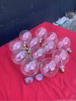 12 clear globe lightbulbs with brass screw bases spread on red fabric, with sunglasses for scale.