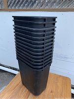 Stacked black plastic office paper garbage cans seen from the side, showing uniform shape and size.