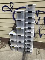 Two stacks of translucent plastic bins with white lids and black latches, stacked outdoors against siding with graffiti.