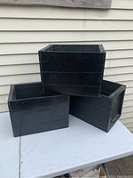 Three vintage black pop crates arranged on white table, showing side views and condition.