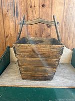 Front view of antique wooden hopper showing rectangular shape with tapering sides and attached wooden handle.