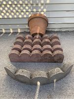 Four reddish-brown rectangular garden edge stones stacked with slotted ends visible and one curved light grey stone in front.