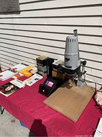 Overview of photographic enlarger, film canisters, expired papers and accessories on red cloth