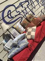 Display of 10 decorative cushions in various colors and patterns alongside a white table lamp with a pleated fabric shade, arranged on a red cloth.