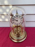 Front view of Kundo mechanical clock with glass dome and brass accents.