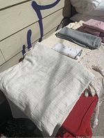 Stack of folded linens including white Jordrok down pillows, light grey and lavender fitted sheets, cream textured chenille bedspreads underneath.