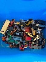 Top view of a large collection of older die cast cars and trucks including buses and construction vehicles in a plastic container