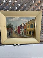 Full view of the framed oil painting depicting a French street scene with buildings, a church, and a lone figure walking on the street.