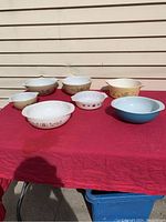 All seven Pyrex bowls and servers arranged on a red cloth with assorted vintage patterns and colors.