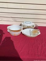 Eight Pyrex pieces arranged on red cloth including casseroles, divided dishes, and lids