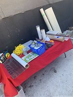 Photo of a variety of renovation supplies on a red table including rolls of ventilation mesh, window film, and electrical junction boxes.