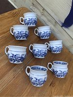 Eight porcelain coffee cups arranged showing their Blue Onion pattern and scalloped rims.