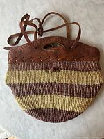 Full view of the sisal handbag showing woven yellow and brown stripes with large rustic leather handle.