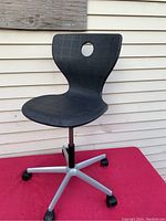Front view of black Verner Panton Panto Lupo office chair on red surface against exterior wall.