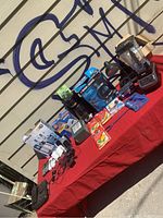 Overview of the lot on a red tablecloth showing a blender, coffee maker, packaged chargers, headphones, and other small items.