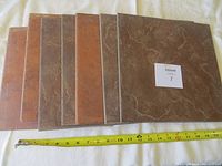 Seven ceramic tiles arranged overlapping in a row on a white surface with a measuring tape in front showing approximate tile width of 12 inches.