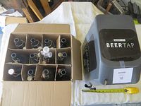Box with 12 brown glass bottles, some fitted with airlocks, and Beer Tap dispensing device beside it