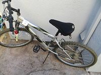 View of the full left side of the silver Rallye Incline mountain bike showing frame, seat, pedals, handlebar, and front tire.