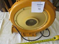 Front view of yellow air blower showing air intake with metal grille and base mount, electrical cord visible.