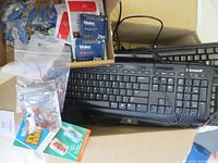 Wide shot showing Microsoft wired keyboard with cable coiled on top, multiple small circuit boards, packaged and loose electronic parts inside a cardboard box.