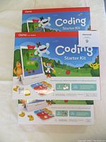 Photo displaying three unopened Osmo Coding Starter Kit boxes stacked with front-facing view showing kit name, colorful cartoon animal characters, and iPad stand illustration.