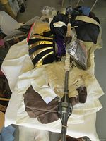 Pile of mixed costume pieces including Egyptian-themed black and gold headdress, white and brown fabrics, and a staff or prop weapon.