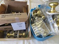 Boxes and containers holding several used door knobs and parts including brass knobs, clear glass knobs, and assorted metal components.