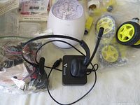 Black headset with microphone and cables, white dome gadget with designs, yellow wheels and other small parts visible