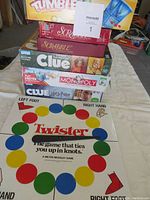 Photo showing stacked board game boxes: Tumble, Scrabble, Clue, Monopoly, Twister mat laid out