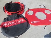 Rukket Golf practice net, red target panel with three holes, and carry bag laid out on concrete.