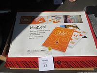 Closed box of GBC HeatSeal laminating pouches showing label with product details and sample laminated sheets in use.