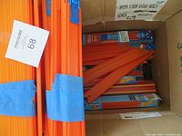 Box with multiple bright orange Hot Wheels track pieces bundled with blue tape and partially packed inside a cardboard box along with boxed track pieces.