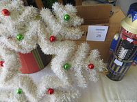 White Christmas wreath decorated with red and green small balls, set near a red pot and a nutcracker figure.