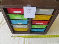 Wooden frame organizer with 10 plastic drawers of various colors labeled with contents and measuring tape indicating width.