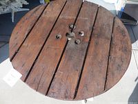 Close-up of the round wooden spool top showing the dark stain, plank construction, central hole, and visible bolts.