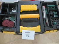 Top view of a black and yellow carrying/storage case with multiple compartments containing various plastic gears and metal brackets for Vex robotics parts.