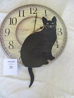 Photo of round wall clock with a black cat silhouette on the face and a pendulum tail below. Clock design shows Arabic numerals and minute markings on a rustic wood-like background.