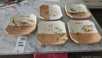 Five Asian pottery plates displayed on marble surface showing overall set and handpainted details with calligraphy.
