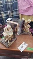 Two ceramic bookends with seated and crouching figure, glass bowls behind, candle partially visible