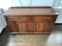 Front view of antique hardwood buffet showing two drawers and double cabinet doors with carved patterns and metal drawer pulls